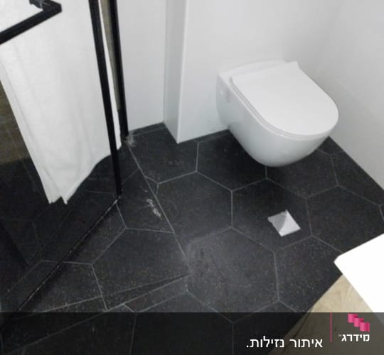 רצפת חדר אמבטיה עם אריחים כהים ונזילה